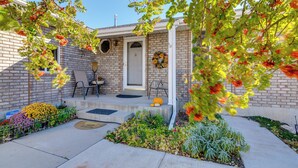 A brick house with a front porch, a door, and a small garden with various plants and flowers.