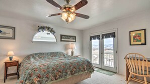 A bedroom with a bed, a ceiling fan, a chair, a lamp, a window, and a door.
