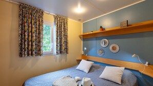 A bedroom with a bed, a window with curtains, a bedside table, a lamp, and wall decorations.