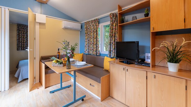 A compact kitchenette with a TV, a dining area with a table and chairs, and a sofa.