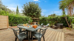 An outdoor patio with a table set for dining, surrounded by greenery and a wooden deck.