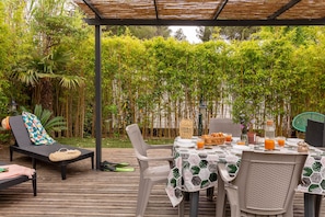 Uma área de refeições ao ar livre com uma mesa posta para dois, rodeada por folhagem de bambu.