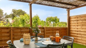 An outdoor patio with a table set for two, surrounded by a wooden fence, and a view of a garden with various plants and trees. - Estrellus, mobile home in the vineyard (Hyères)