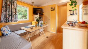 A compact living space with a sofa, dining table, kitchenette, and a television. - Estrellus, mobile home in the vineyard (Hyères)