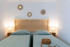 A bedroom with two beds, a woven headboard, bedside lamps, and decorative wall mirrors.