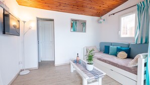Ein gemütliches Zimmer mit Holzbalkendecke, einer Couch mit Kissen, einem kleinen Tisch mit Pflanze und einem Fenster mit Vorhängen.