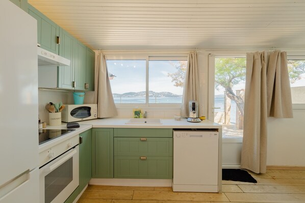 Une cuisine compacte avec vue sur la mer, équipée d’un four à micro-ondes, d’un évier et d’un réfrigérateur.