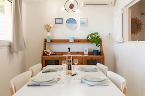Uma sala de jantar com uma mesa posta para quatro pessoas, uma garrafa de vinho e um relógio na parede.