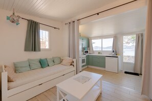 Quarto aconchegante com sofá, mesa pequena, cozinha compacta e vista para o exterior.