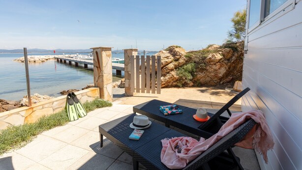 Une terrasse avec vue sur la mer, une clôture en bois et une table sur laquelle se trouvent un chapeau et des lunettes de soleil.