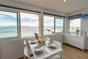 A dining area with a table set for two, large windows with a view of the sea, and a clock on the wall. - La Roche, cottage on the waterfront in La Madrague (Hyères)