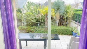 Een terras met een tafel en stoelen, omgeven door diverse planten en uitzicht op een tuin.