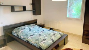 Een moderne slaapkamer met een bed, een hanglamp, een raam met uitzicht op groen en een radiator.
