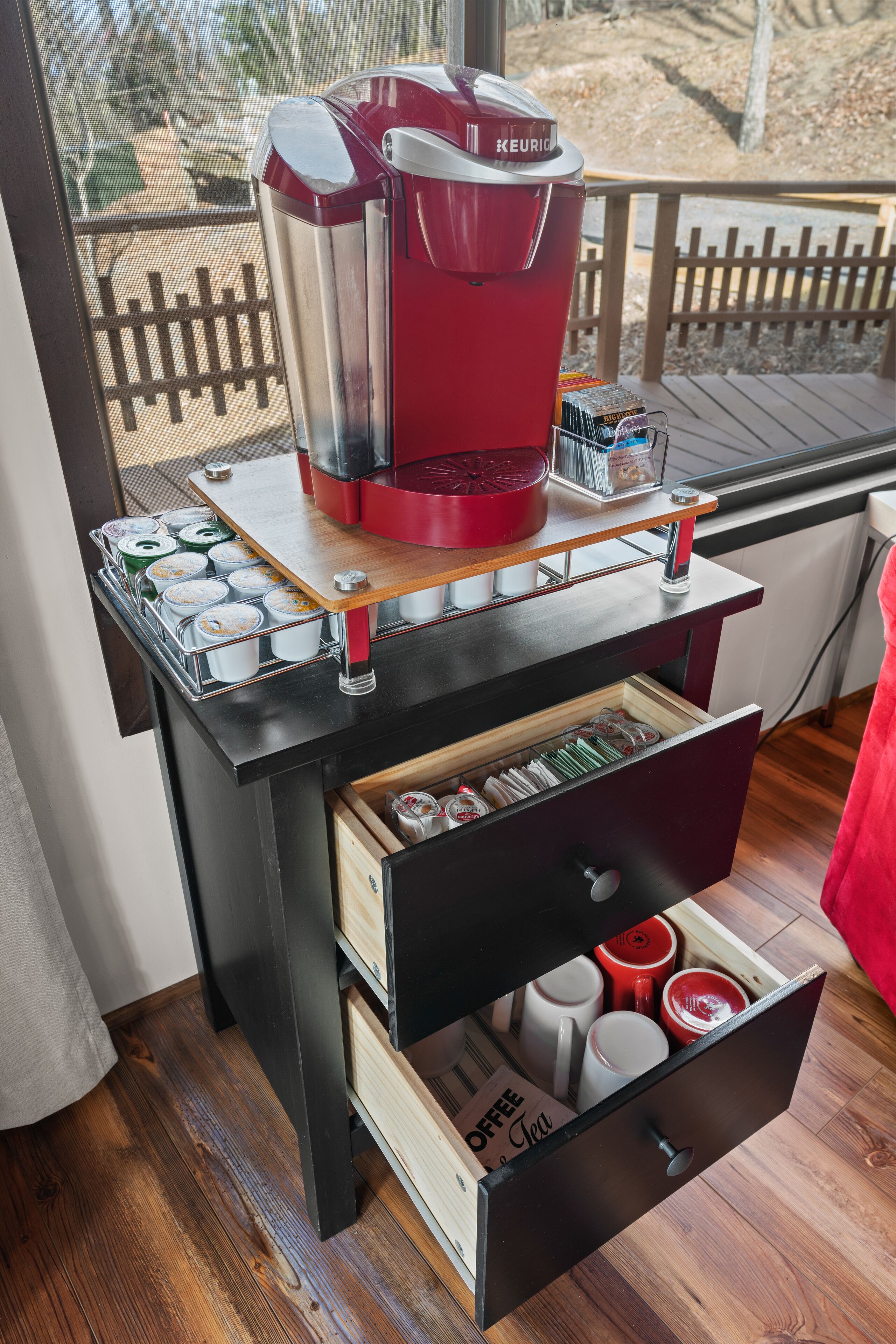 Kahvinurkkaus, jossa on Keurig-kahvinkeitin, tarjoilualusta kahvikuppeja varten ja laatikko, jossa on kahvimukeja.