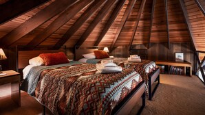 A cozy attic bedroom with wooden beams, two beds, a nightstand, and a reading area. - Fall Foliage Treehouse Getaway with 360 views (Basye)