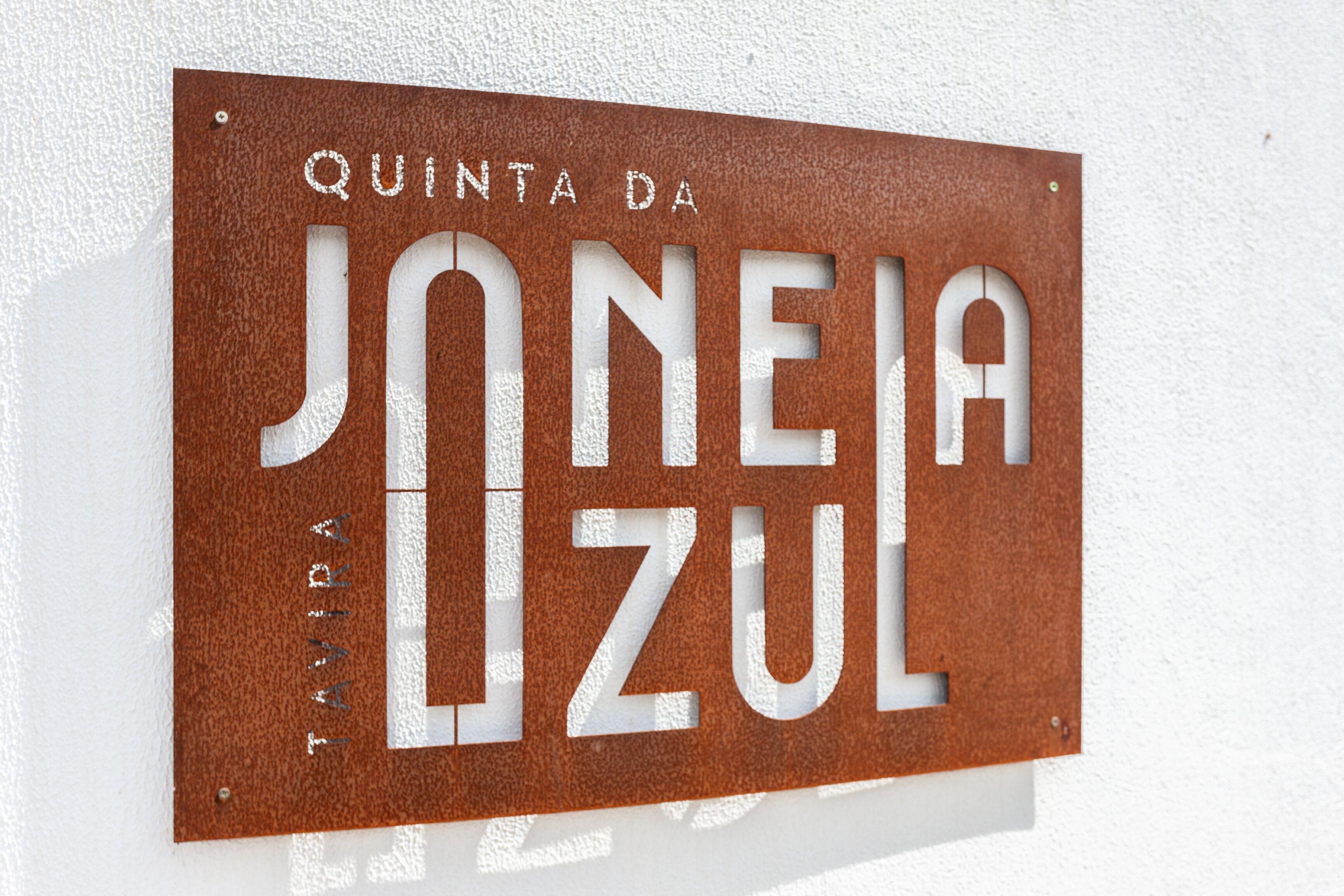 Un letrero con el texto "QUINTA DA JONEJA" y "TAVIRA" sobre un fondo marrón texturizado.