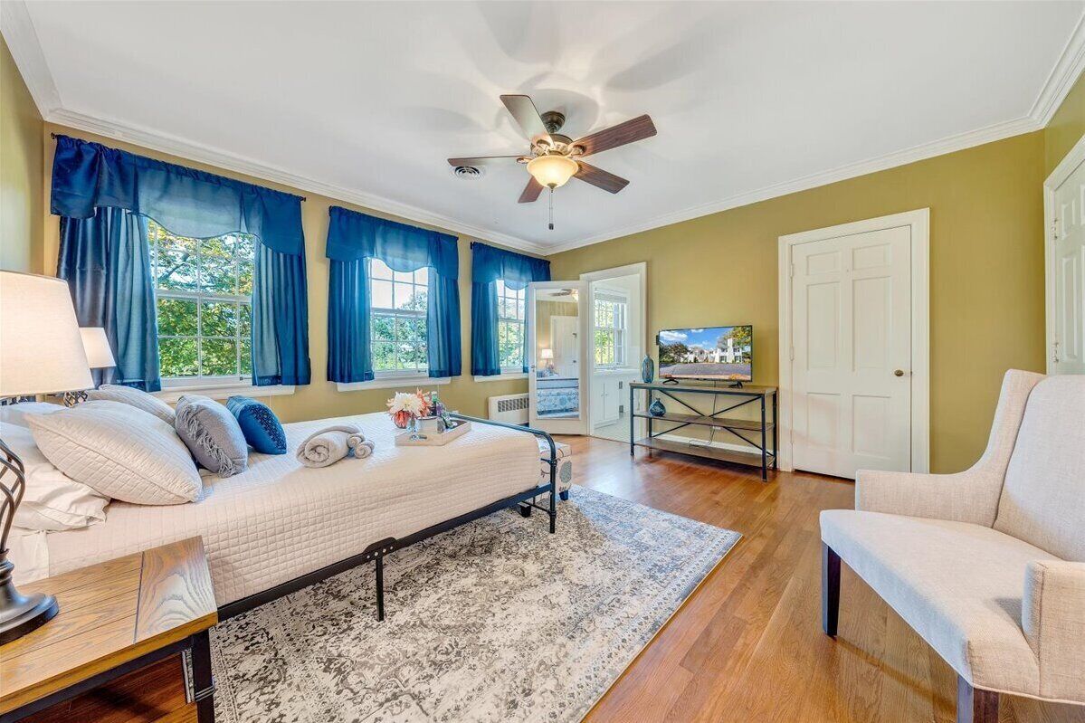 A bedroom with a bed, a desk, a chair, a ceiling fan, and a TV.