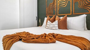 Un lit bien fait, avec une couverture marron, des oreillers blancs et un mur d’accent vert orné d’œuvres d’art abstraites.
