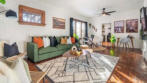 Un salon moderne avec un canapé vert, un tapis à motifs et un coin repas comprenant une table et des chaises.