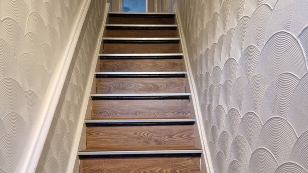 Un escalier en bois, avec un mur à texture de chaque côté.