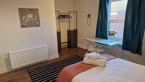 Une chambre à coucher comprenant un lit, un bureau, une chaise, un radiateur, une fenêtre avec des rideaux et un élément de décoration murale.
