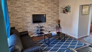 Un salon avec un mur en pierre, un téléviseur à écran plat, une table basse et un canapé.