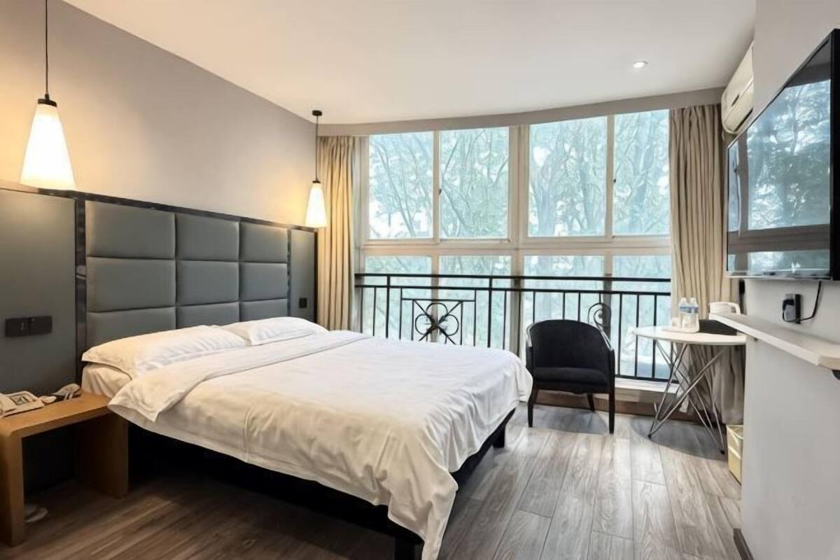 A hotel room with a bed, bedside table, chair, small table, and a window with a view.