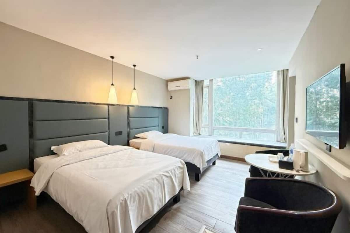 A hotel room with two beds, a small table, a chair, and a TV mounted on the wall.