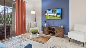 A modern living room with a flat-screen TV, a white sofa, a wooden coffee table, and a glass door leading to an outdoor area. - Cozy Townhome Steps From Clubhouse Amenities! (Kissimmee)