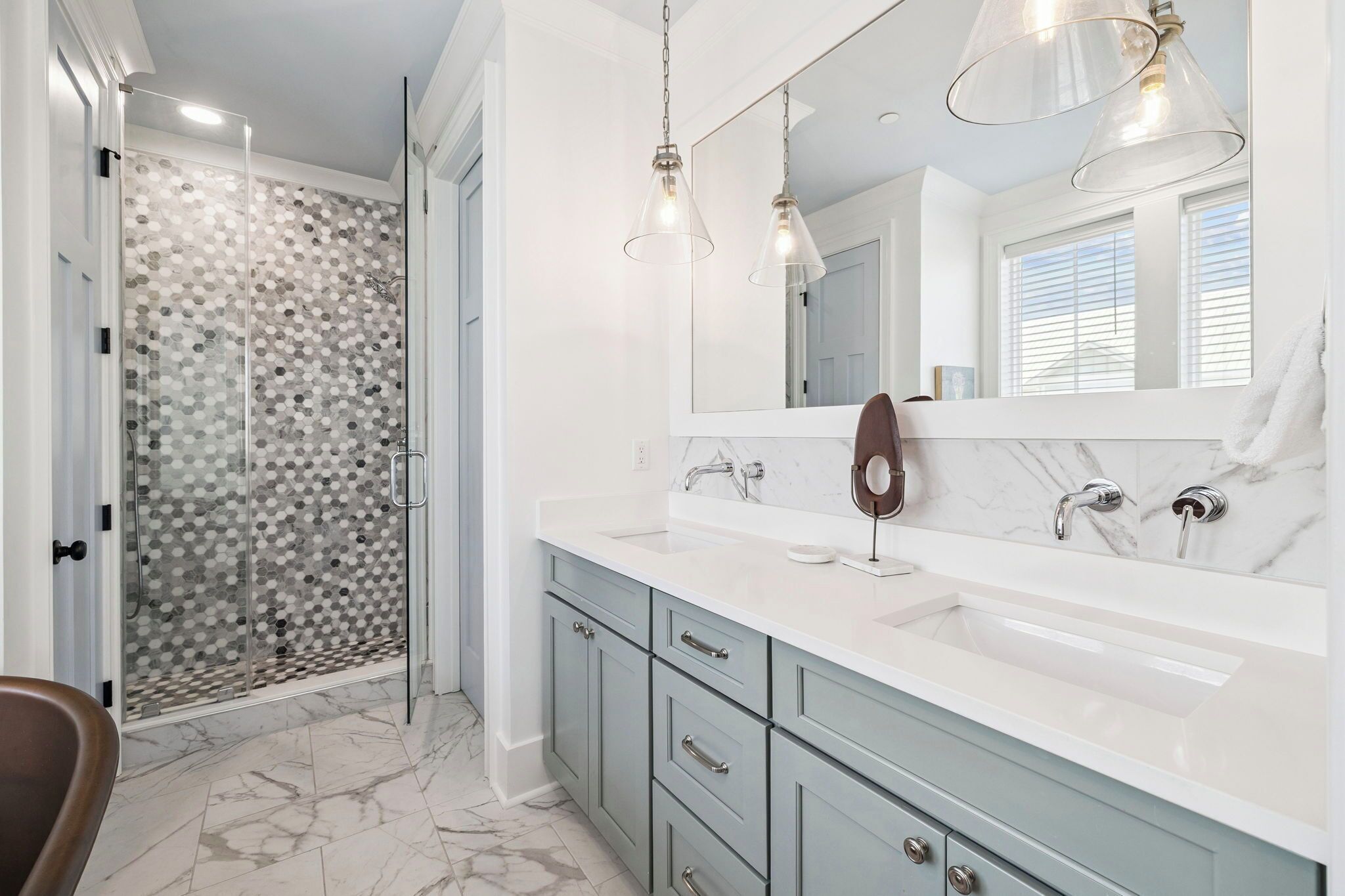 A bathroom with a shower, two sinks, a mirror, and pendant lights.