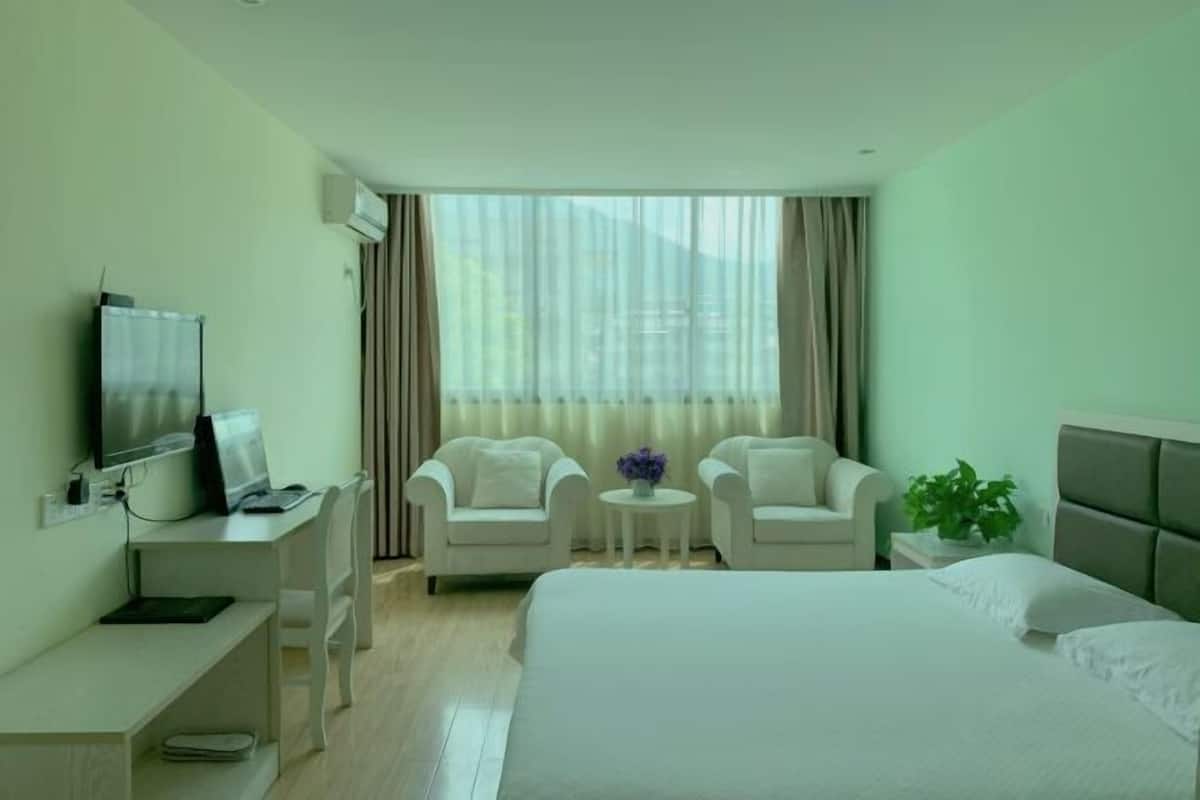 Een hotelkamer met een bed, een bureau met een televisie, twee fauteuils, een kleine tafel met een vaas en een raam met gordijnen.