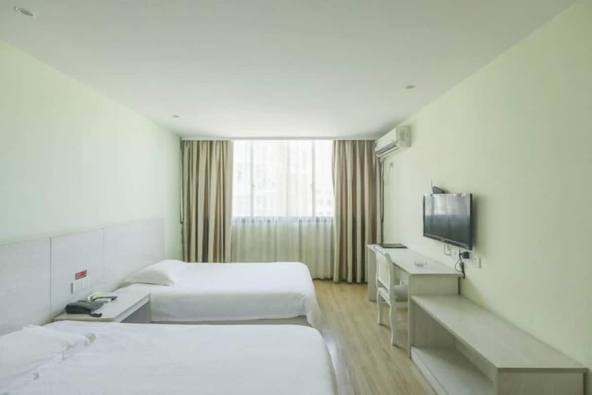 Een hotelkamer met twee bedden, een bureau, een televisie en een raam met gordijnen.