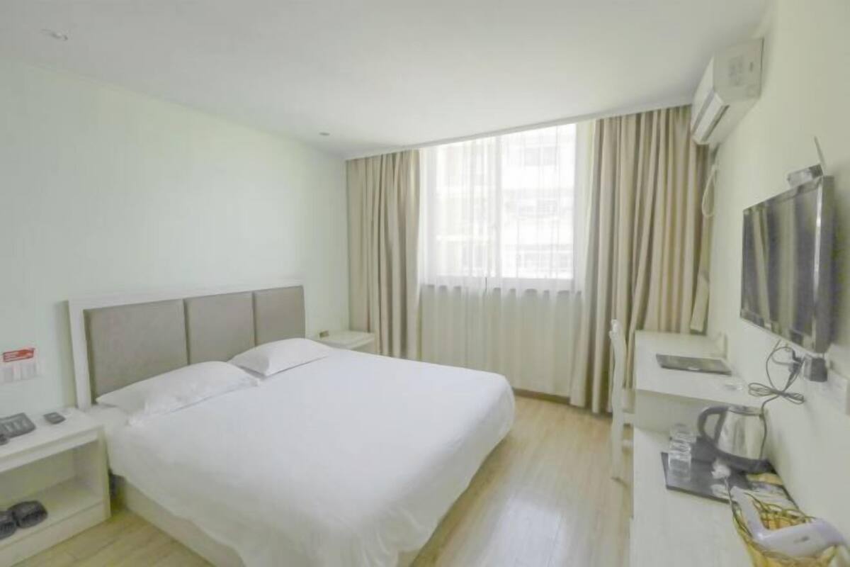 Een hotelkamer met een bed, een televisie, een bureau en een raam met gordijnen.