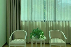 Een kamer met twee witte stoelen, een kleine ronde tafel met een bloempot en dunne gordijnen.