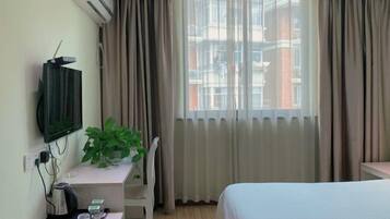 A hotel room with a bed, a desk with a plant, a TV, and a window with curtains.
