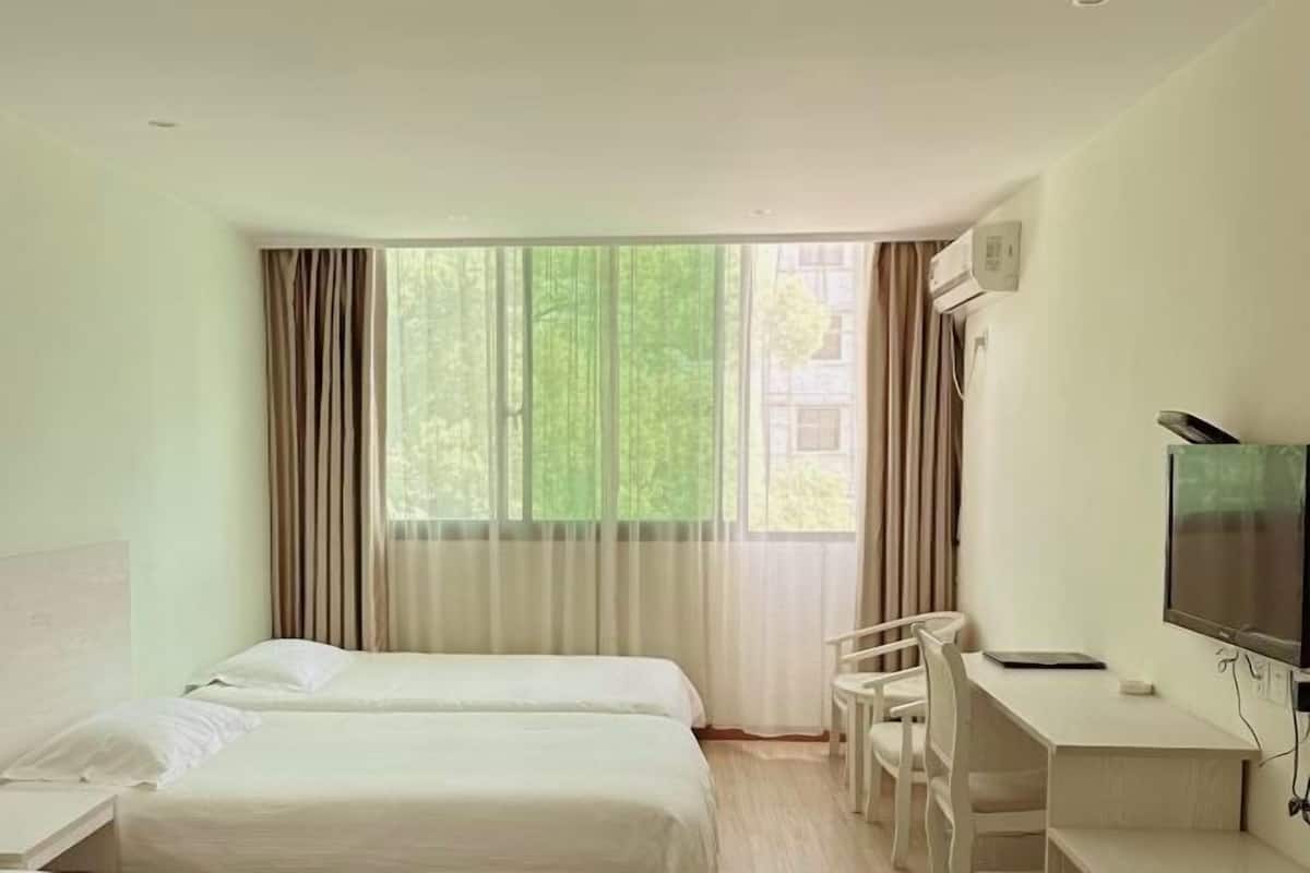Een hotelkamer met twee bedden, een bureau, een stoel, een televisie en een raam met gordijnen.