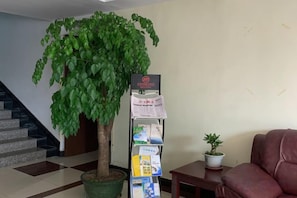 Un espace d’accueil avec une plante en pot, un panneau d’affichage où sont accrochées des brochures, un escalier et un canapé rouge.