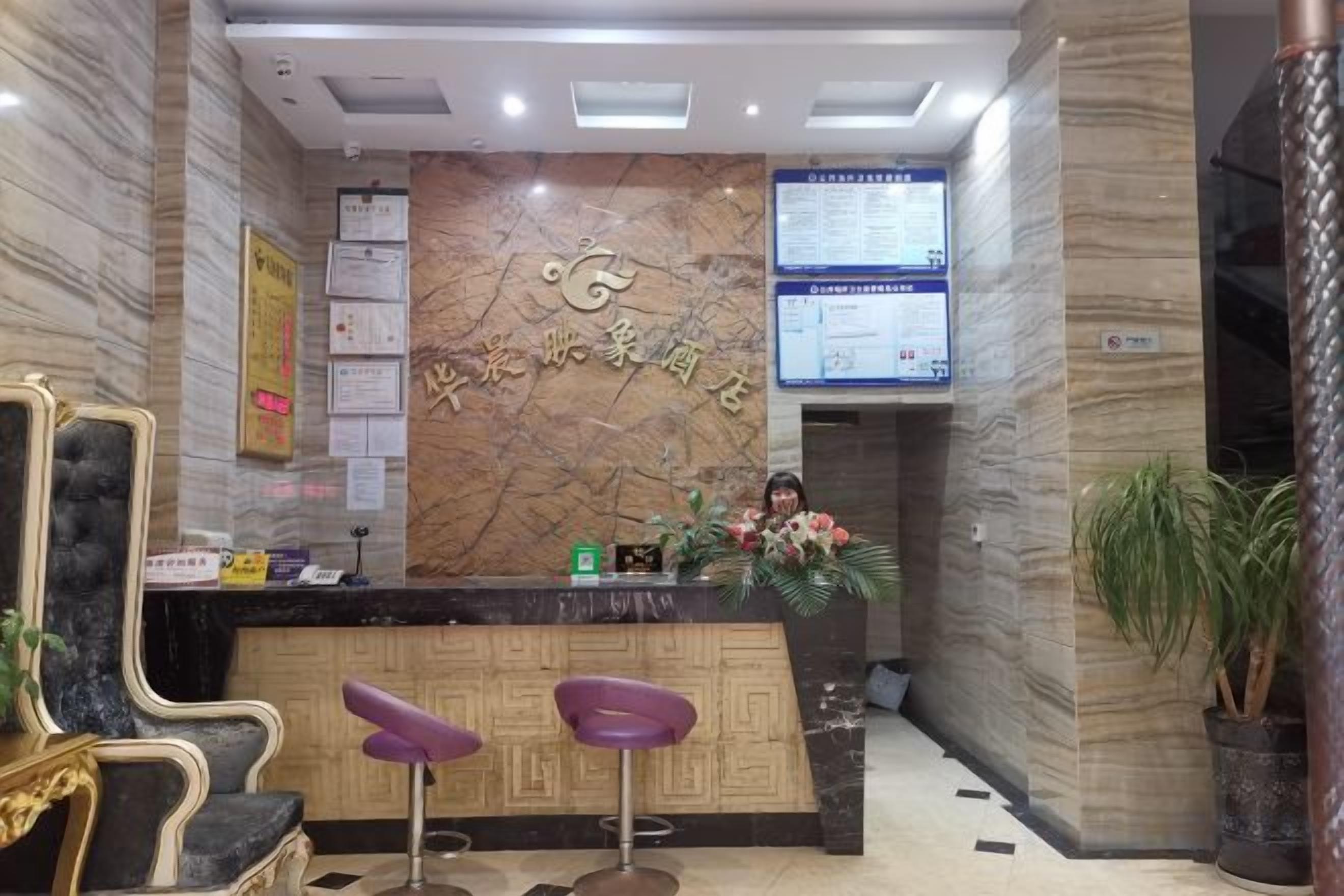 A reception area with a marble wall, a reception desk, two purple bar stools, and a potted plant.