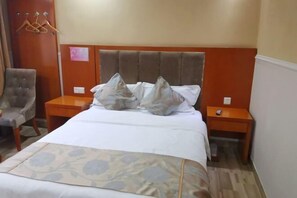 A hotel room with a bed, two nightstands, a chair, and a coat rack. - Yi Long Hua Chen Impress Business Hotel (Yilong)