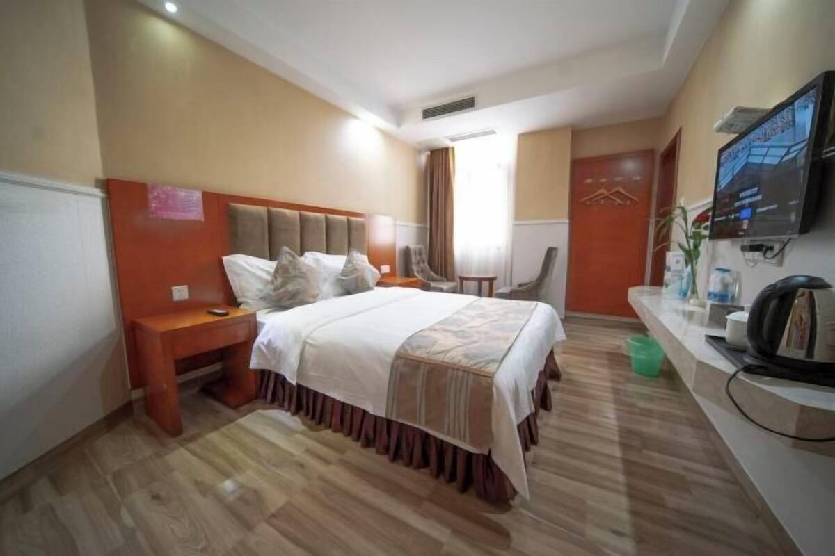 Ein Hotelzimmer mit Bett, Nachttisch, Sessel, Fernseher und kleinem Schreibtisch mit Computer.