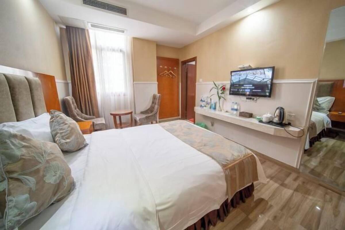 Ein Hotelzimmer mit einem großen Bett, einem an der Wand befestigten Fernseher, einem kleinen Tisch mit Stuhl und einem Spiegel.
