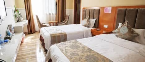 A hotel room with two beds, a desk with a chair, a small table, and a mirror.