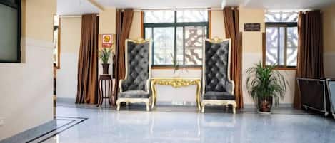 A hotel lobby with a marble floor, two upholstered armchairs, a small table, and a potted plant.