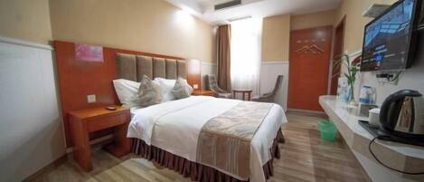 A hotel room with a bed, bedside table, chair, TV, and a desk with a kettle.