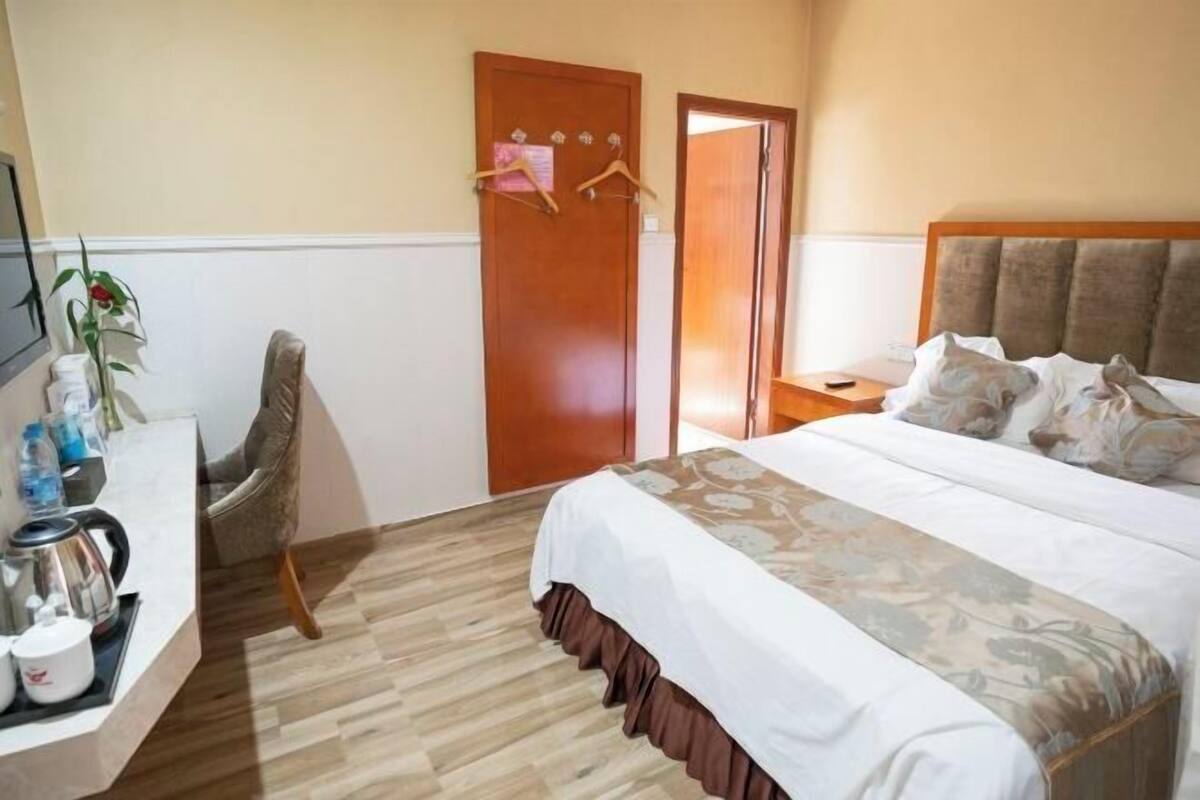 Ein Hotelzimmer mit Bett, Schreibtisch mit Wasserkocher, Stuhl und Tür mit Kleiderhaken.