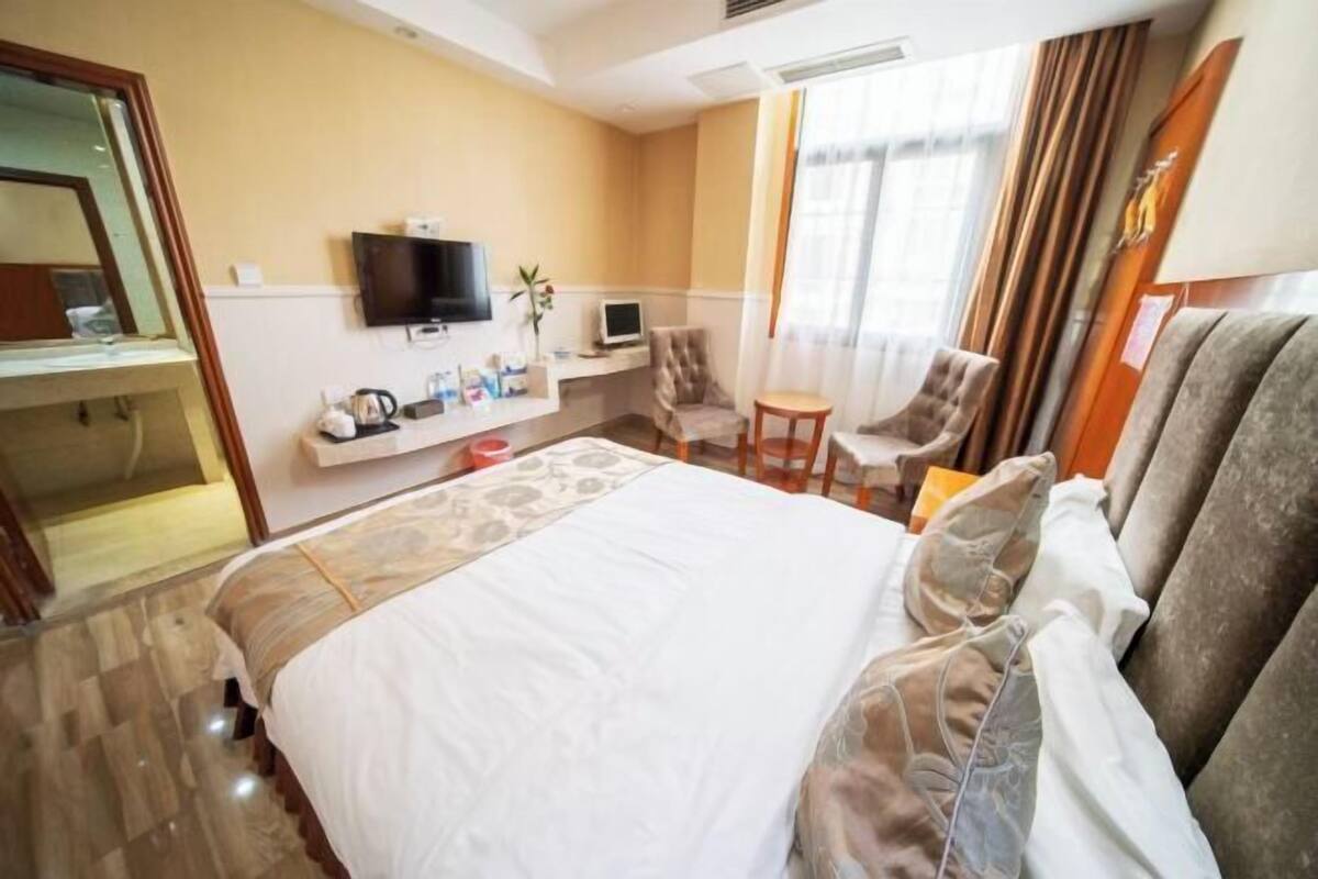 Ein Hotelzimmer mit einem großen Bett, einem Fernseher, einem Schreibtisch mit Computer, einem Sessel und einem kleinen Tisch.