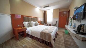 A hotel room with a bed, bedside table, chair, desk, television, and a window.