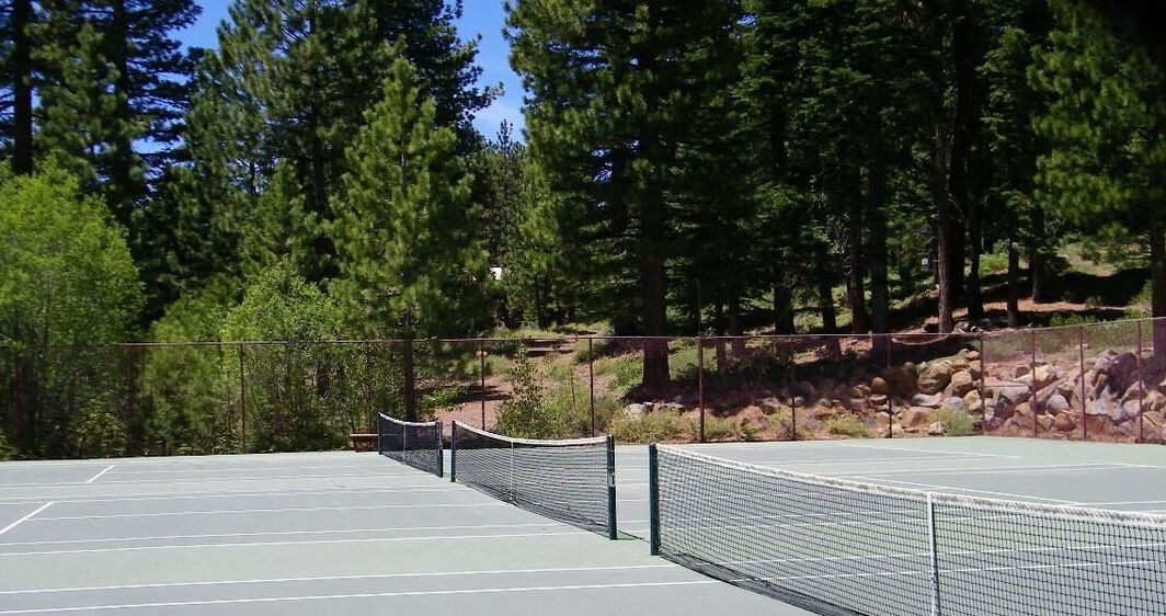 An outdoor tennis court with a net, surrounded by trees and rocks.