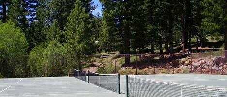 An outdoor tennis court with a net, surrounded by trees and rocks.