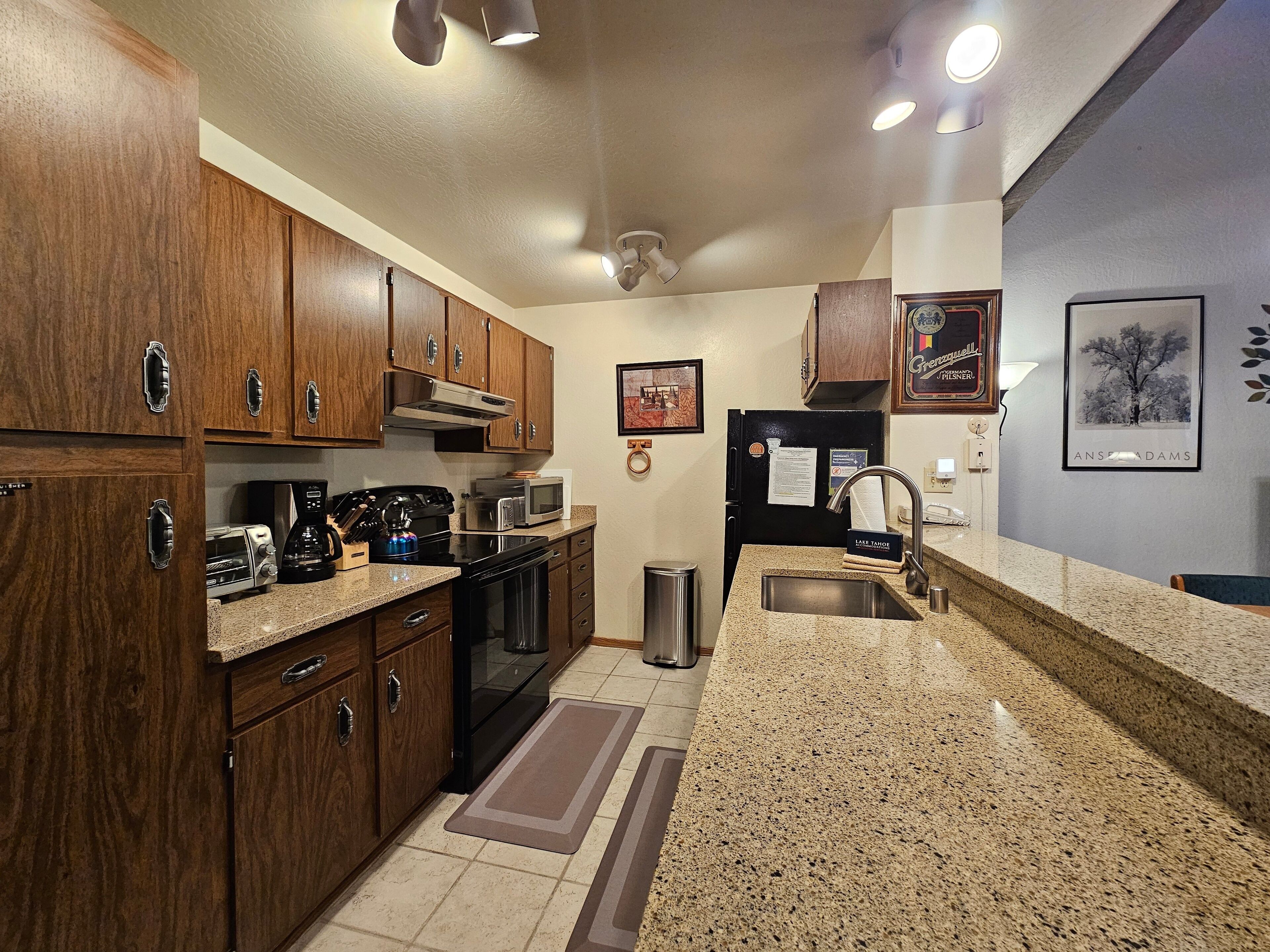 A kitchen with wooden cabinets, a black refrigerator, a microwave, a toaster, and a sink.